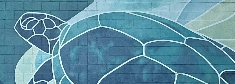 A sea turtle painted in white outline across the blue and green mural on the hotel's wall